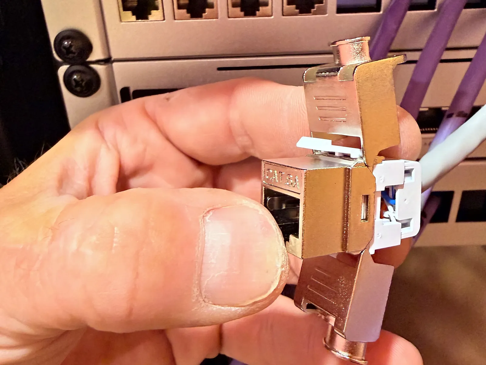 A shielded Cat 6A keystone connector being fitted by hand at the rack