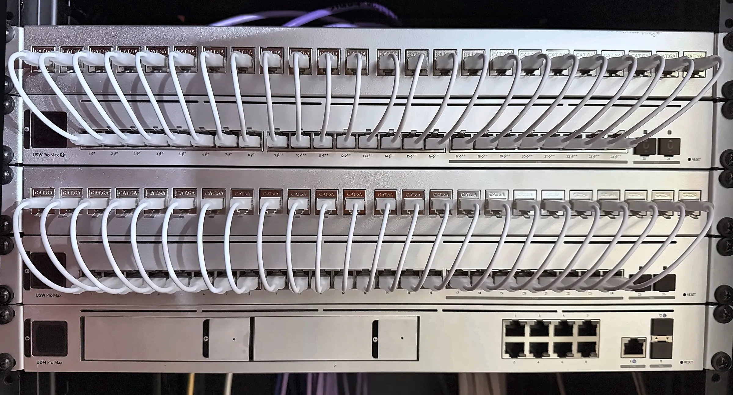 A network rack built by Halo: a UniFi Dream Machine Pro Max gateway beneath two UniFi switches, every port patched with short white leads