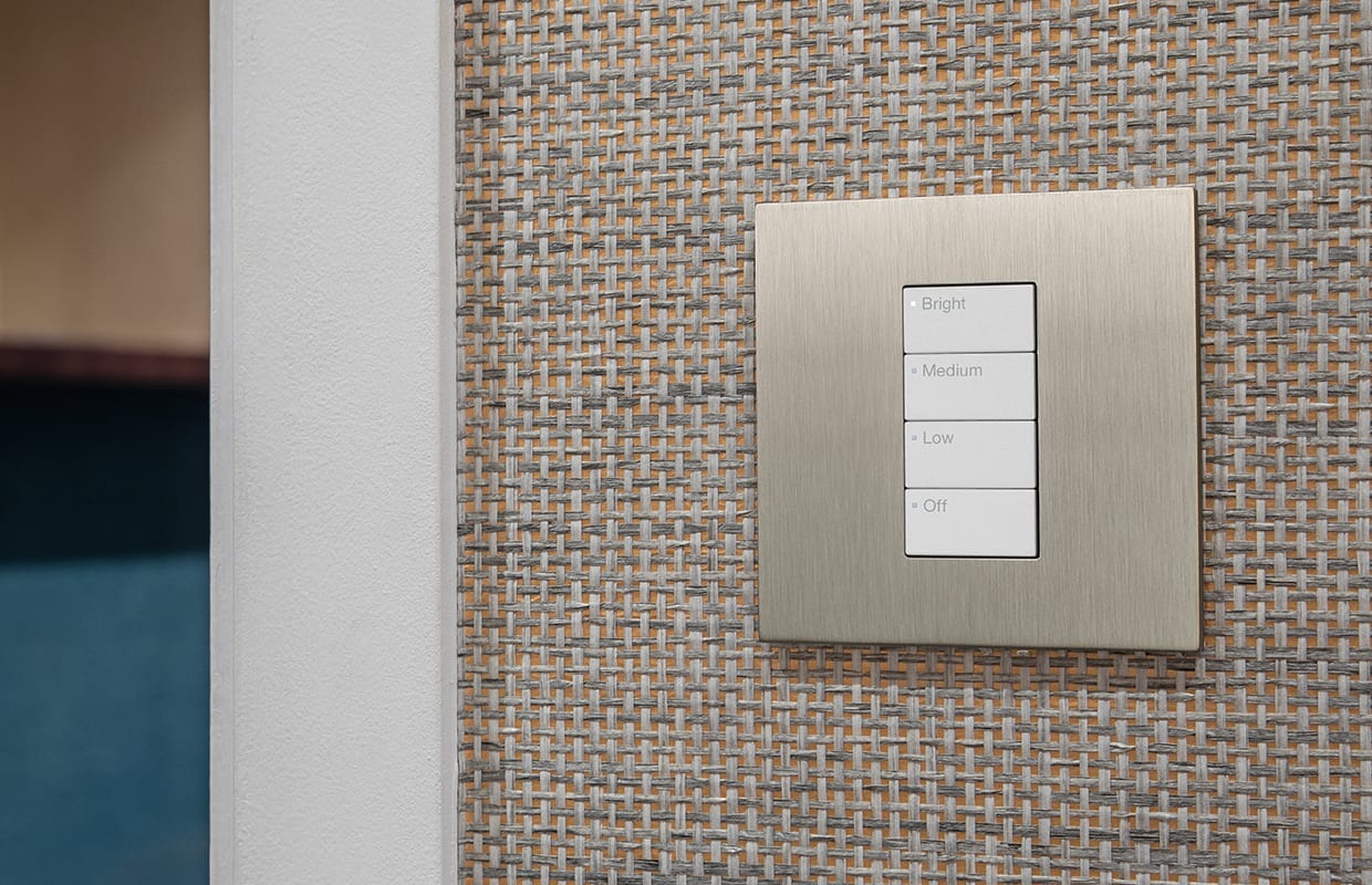 A nickel lighting keypad on a woven grasscloth wall