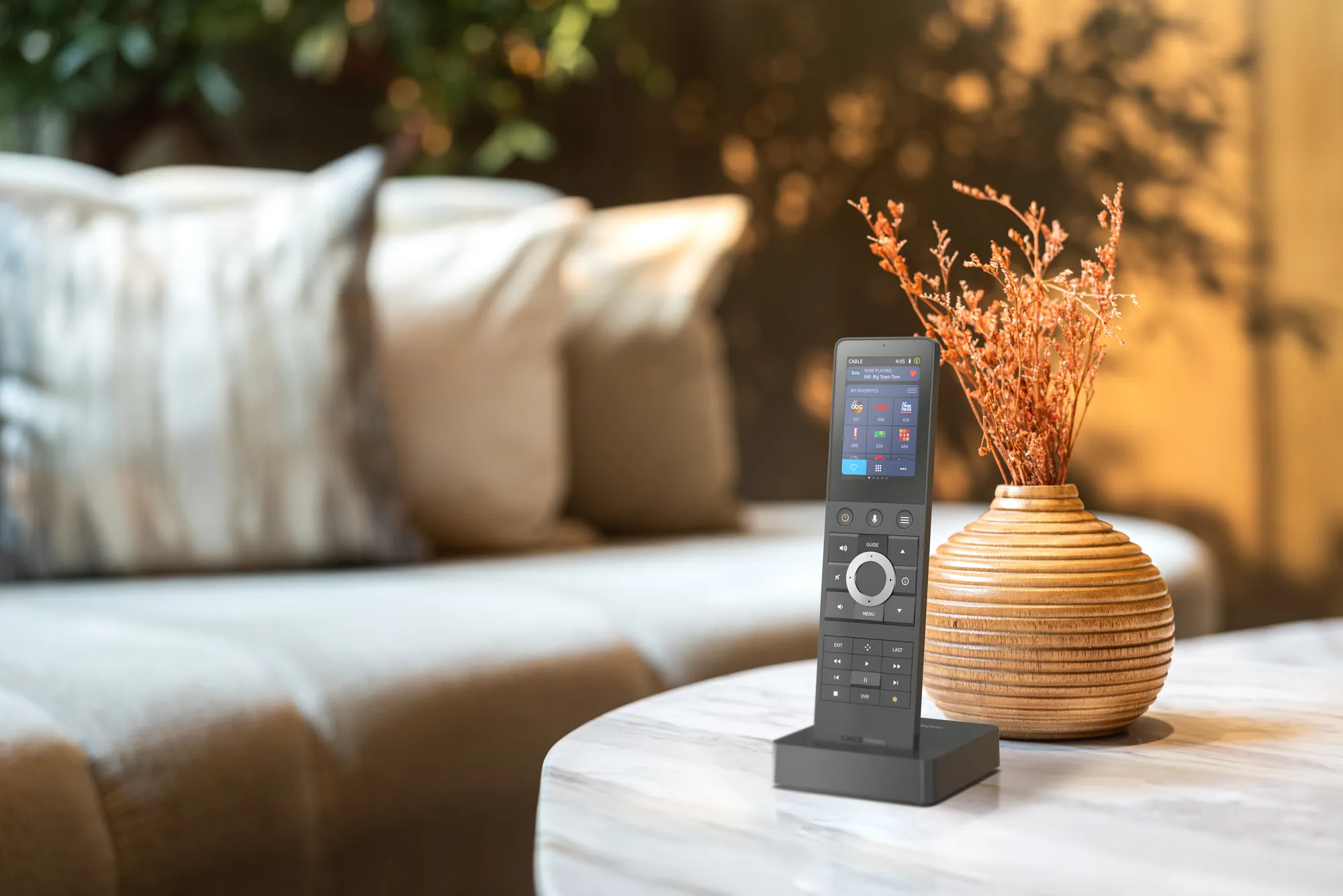 A slim handheld remote with a colour screen, docked on a marble coffee table beside the sofa