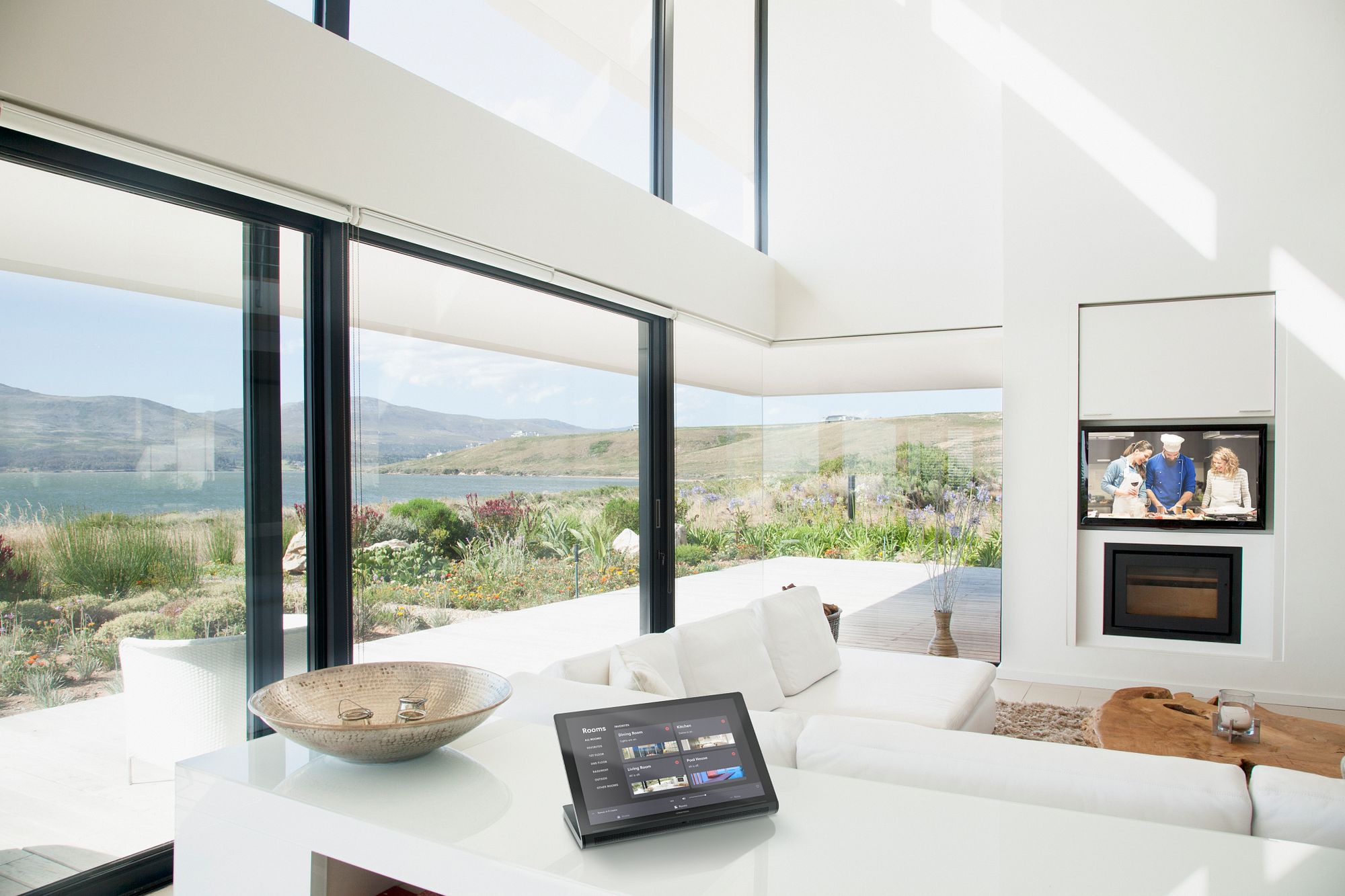 An open-plan living space with a control screen listing rooms across the property, including the pool house