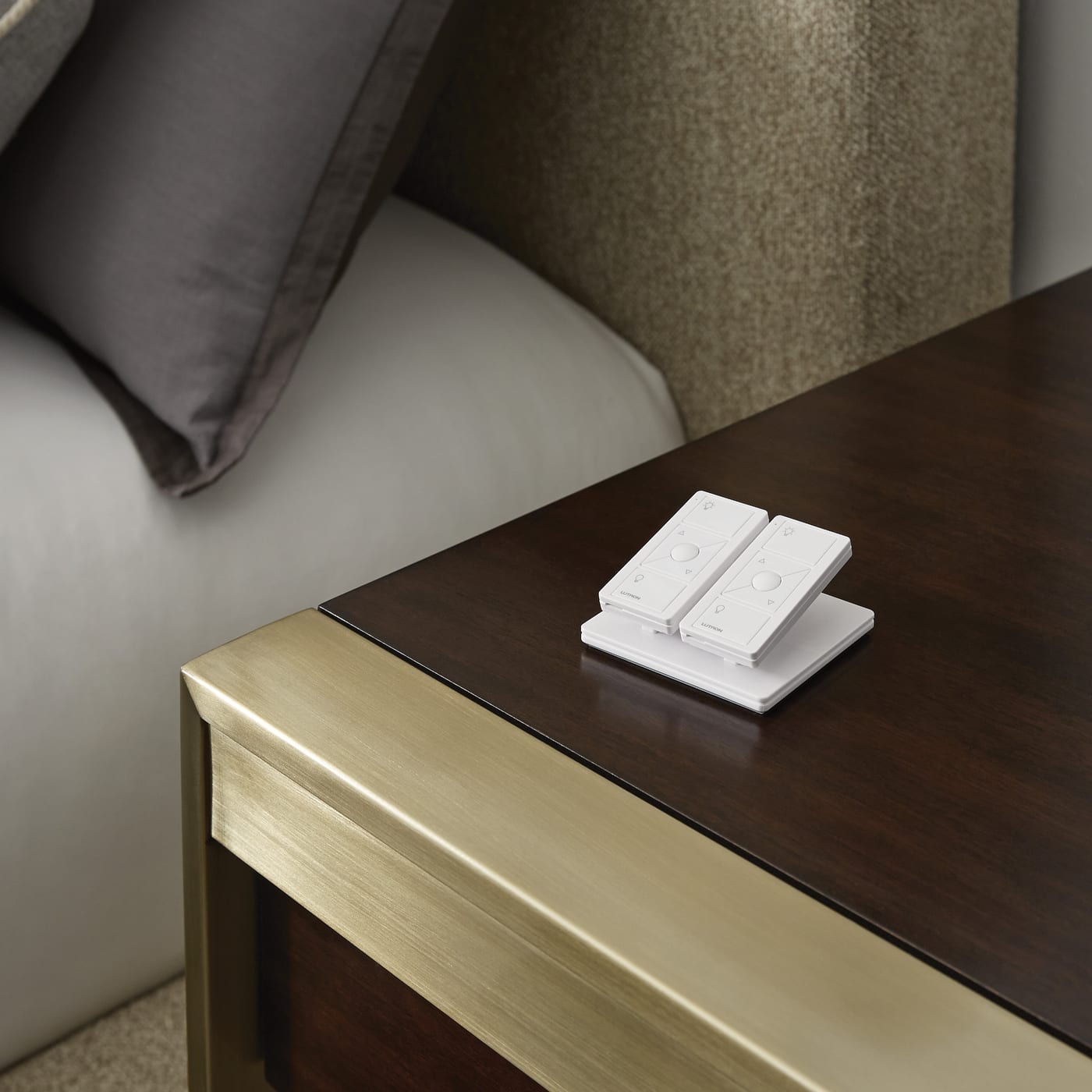 Two white wireless lighting remotes on a walnut nightstand
