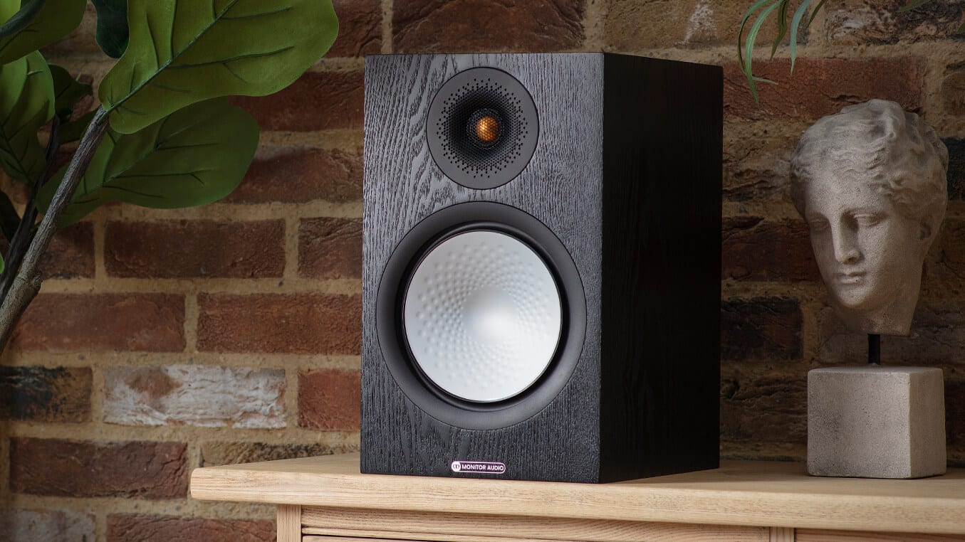 A bookshelf loudspeaker on a wooden console against a brick wall